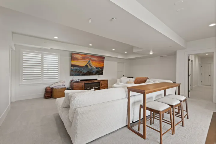 Spacious entertainment area featuring recessed lighting, light-colored carpeting, white plantation shutters, a contemporary media console with a built-in fireplace, and a large wall-mounted television