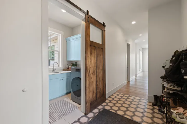 Entryway featuring hexagonal floor tiling, wood-finish flooring, recessed lighting, and a sliding wood-panel barn door with an integrated window, opening to a laundry area with light blue cabinetry
