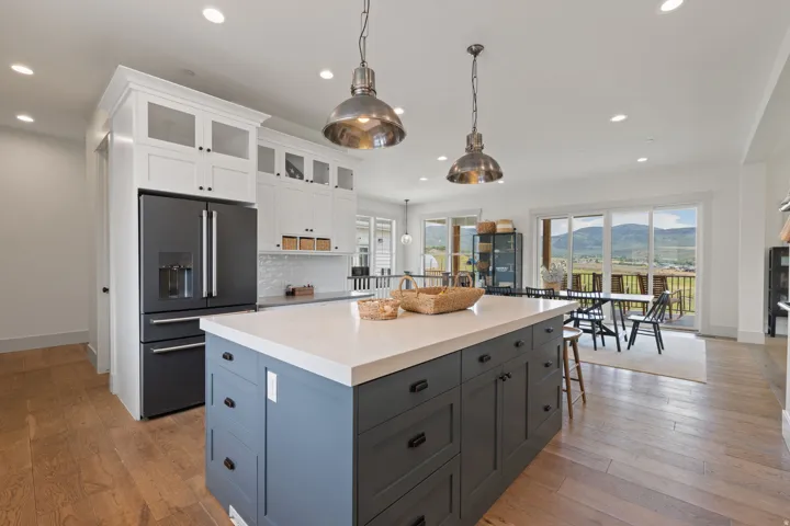 Spacious kitchen featuring a large central island with light-toned countertop, white upper cabinetry with glass-front doors, dark-toned lower cabinetry, and wood-finish flooring