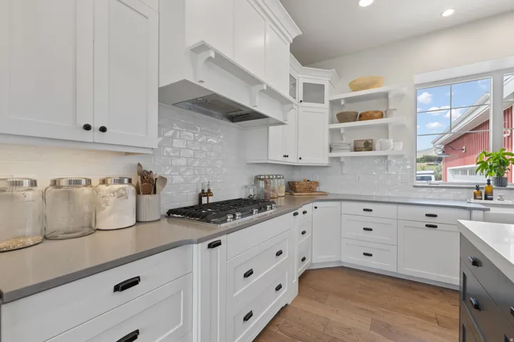 Open kitchen featuring white cabinetry, grey countertops, a gas range with a stainless steel vent hood, and wood-finish flooring