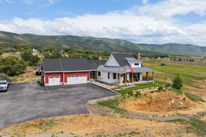 White farmhouse-style residence featuring a covered front porch with exposed timber posts, a dark asphalt shingle roof, and a stone chimney