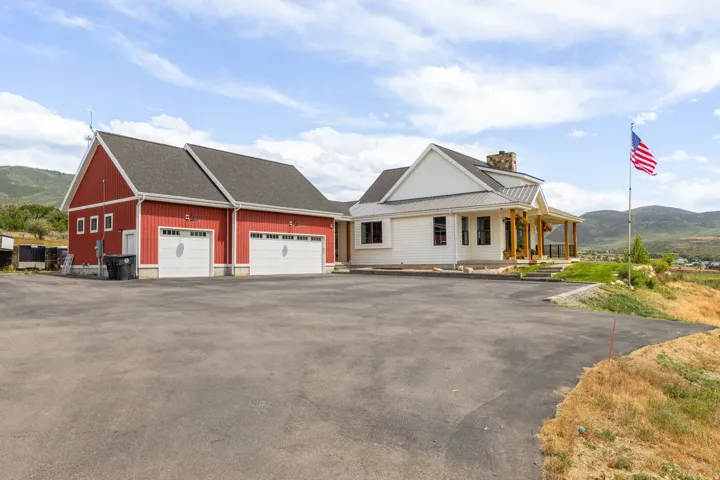 Expansive asphalt driveway providing access to a two-car garage with white paneled doors and a separate red-sided outbuilding with two additional garage doors
