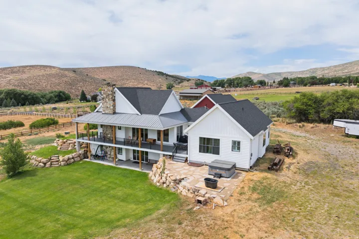 Modern farmhouse exterior with a dual-level porch, stone chimney, and an expansive lawn