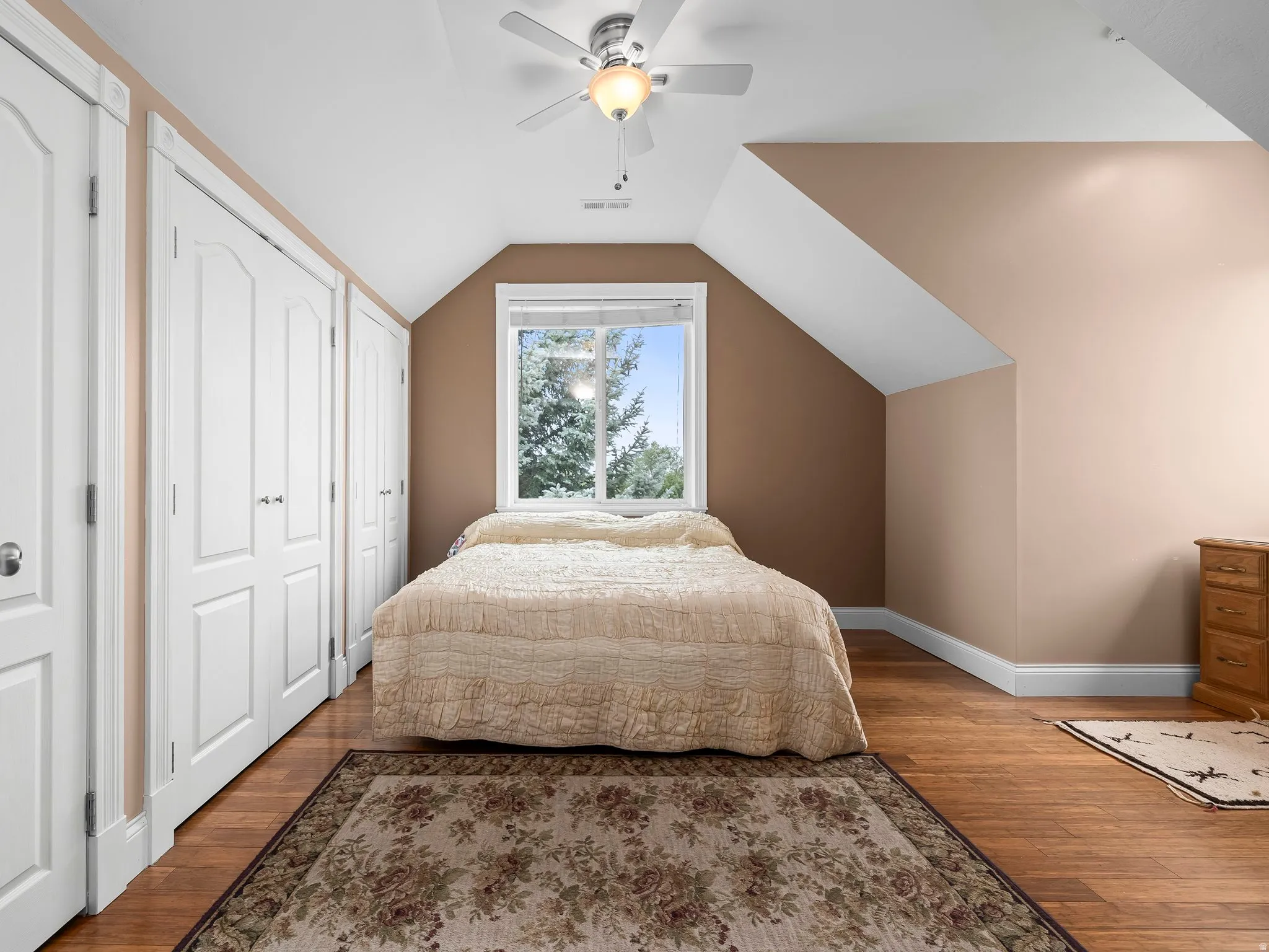 ADU bedroom  featuring wood-finish flooring, multiple white paneled closet doors, a ceiling fan with integrated lighting, and a window providing natural light