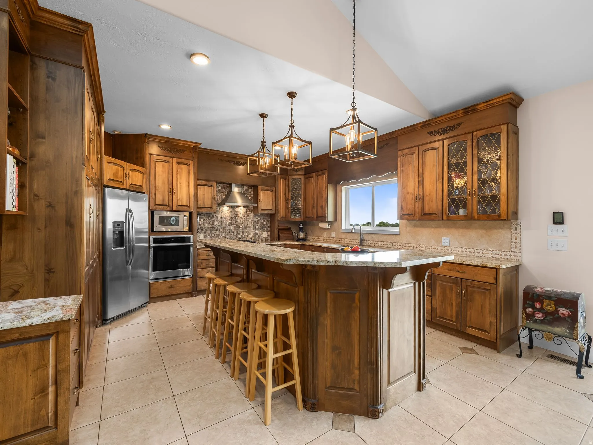 Gourmet kitchen featuring custom wood cabinetry, stainless steel appliances, a large center island with seating, granite countertops, and tile flooring