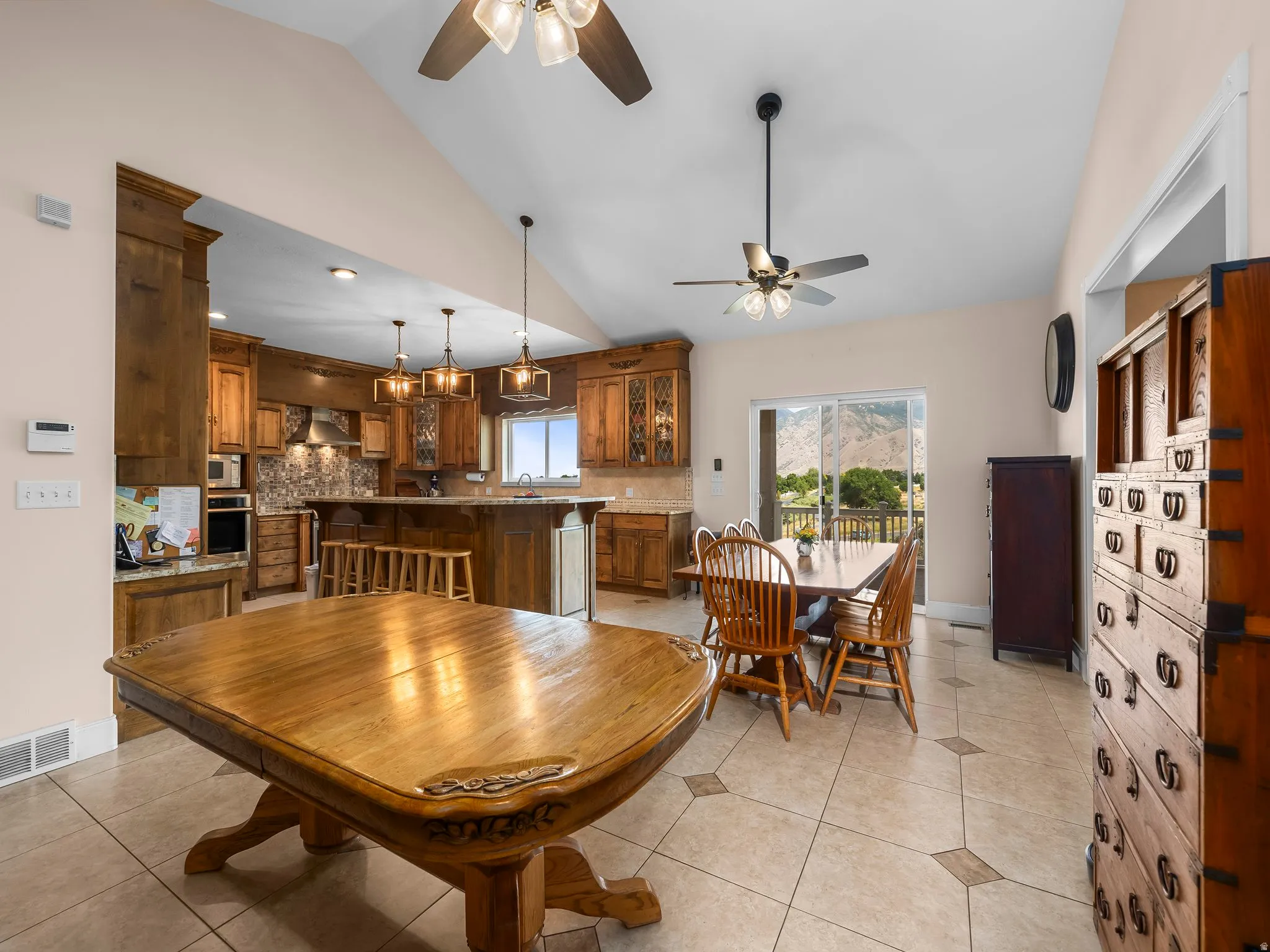 Spacious open concept living area featuring vaulted ceilings with ceiling fans, tile flooring with decorative inserts, and wood-finish cabinetry throughout