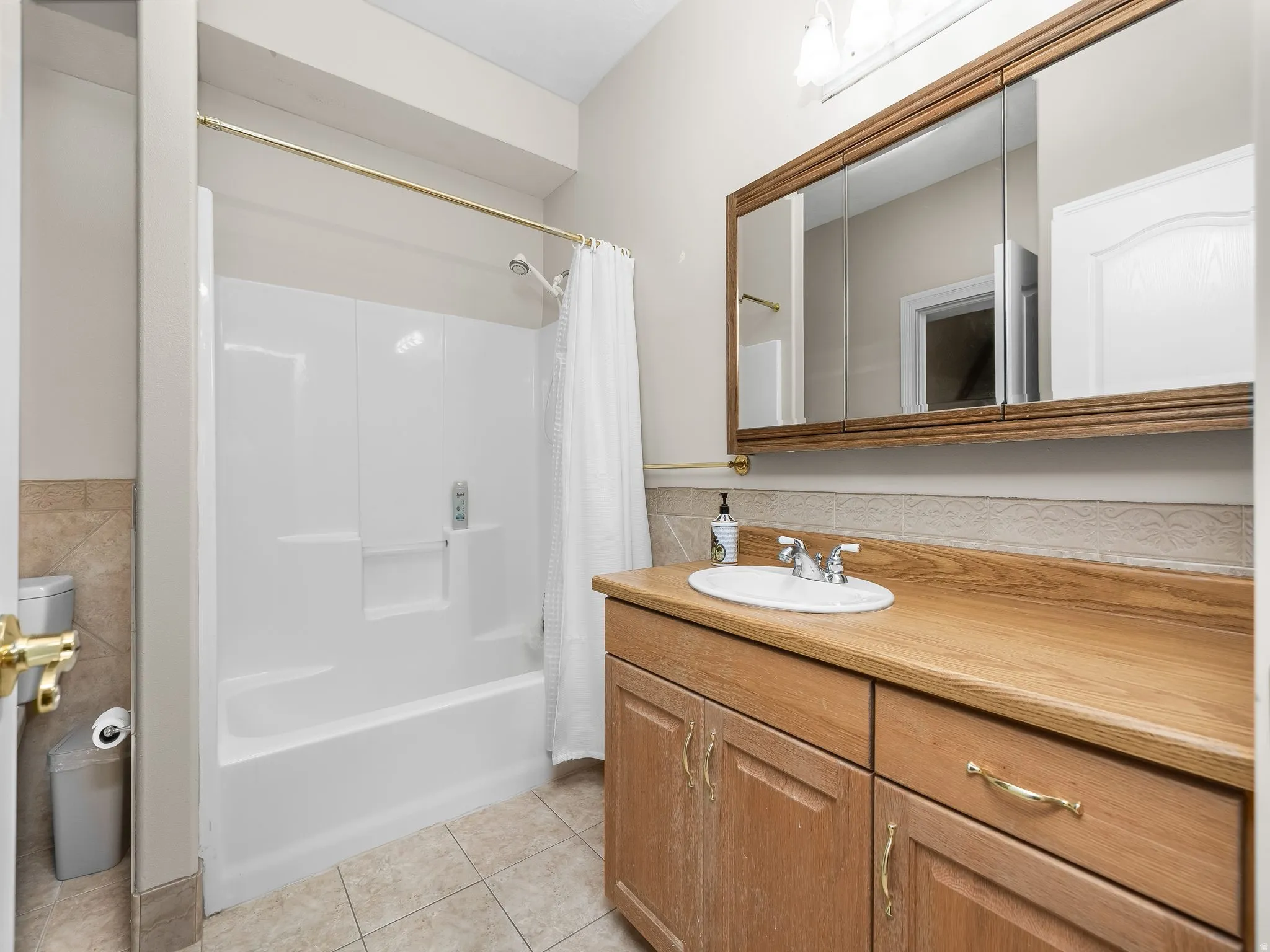 Bathroom featuring a wood-finish vanity with an integrated sink and chrome fixtures, complemented by a triple mirrored medicine cabinet with a wood-finish frame