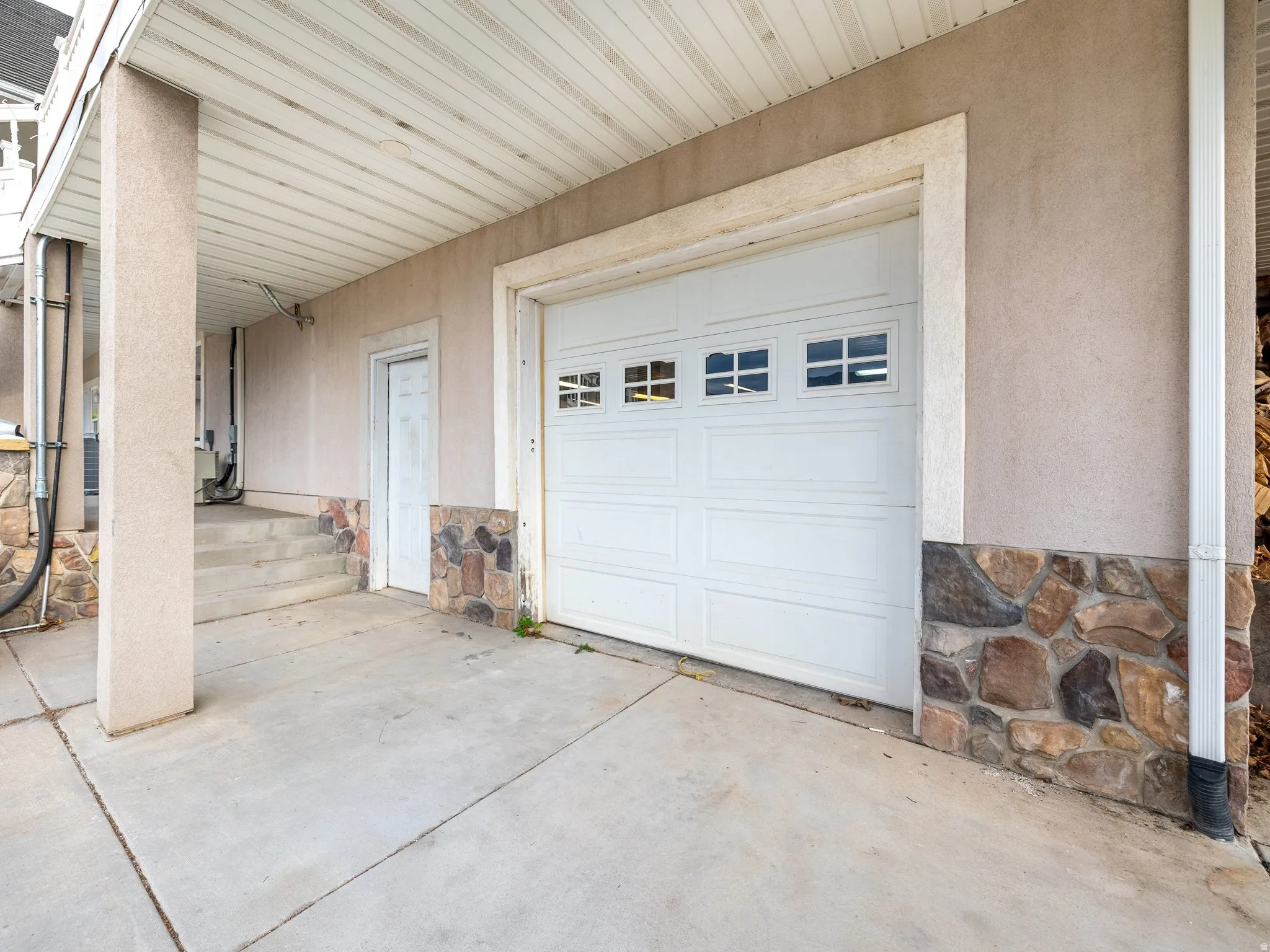 Attached garage with a white panel door and upper window inserts, complemented by a stone veneer foundation and stucco exterior