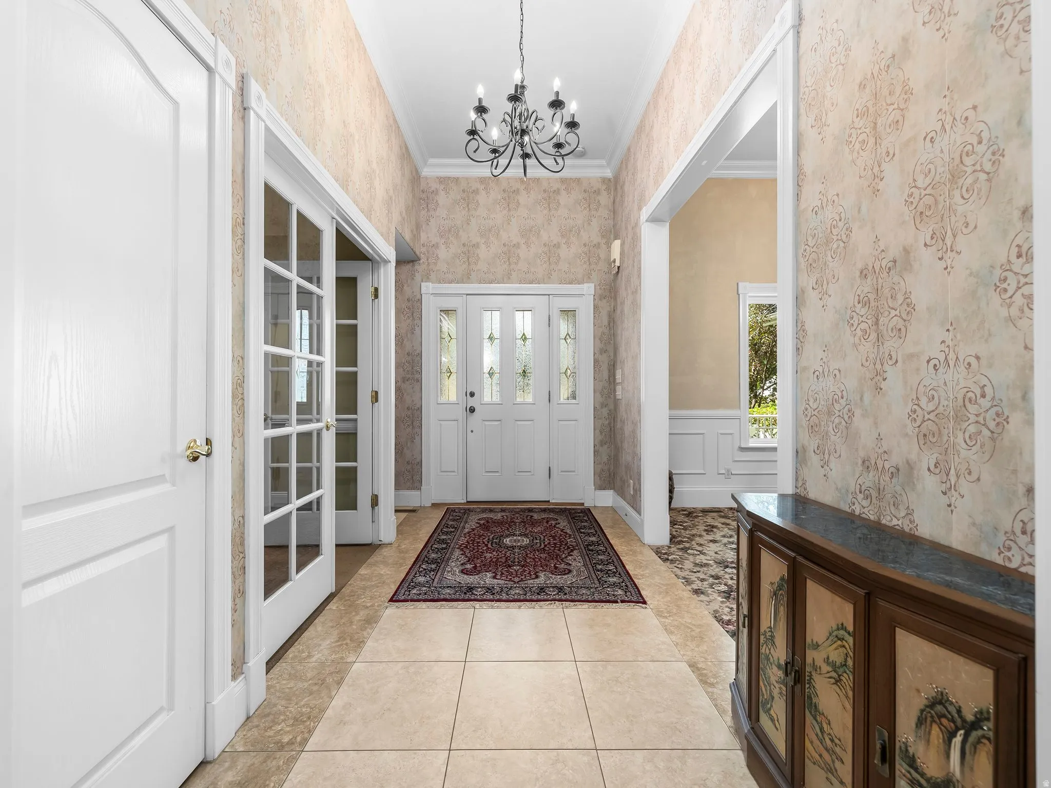 Gracious foyer featuring tiled flooring, decorative wall coverings, a two-panel entry door with sidelights, and a classic chandelier