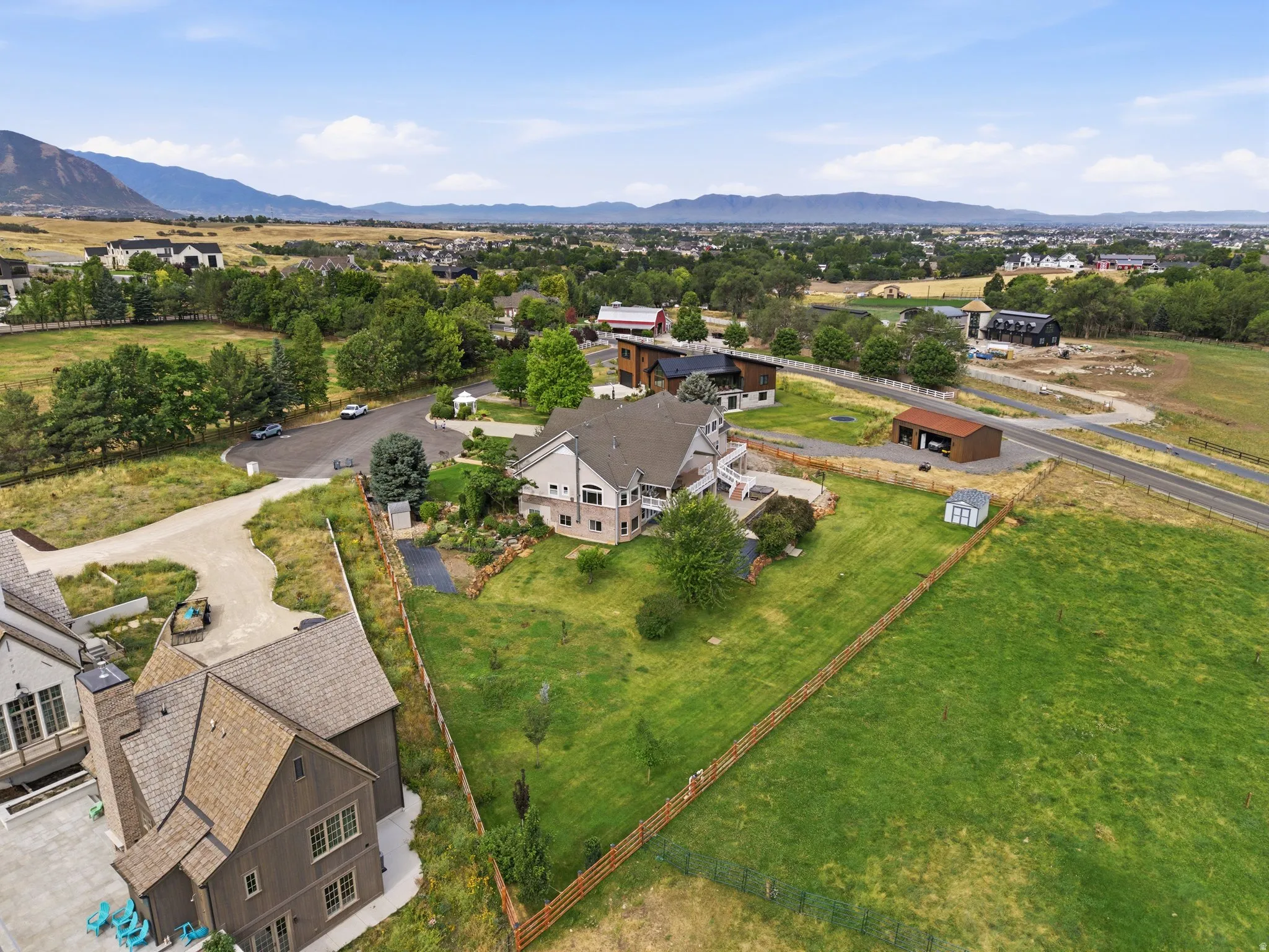 Spacious property featuring a large residence with multiple balconies, an expansive fenced lawn, an accessory building, and a separate detached garage structure