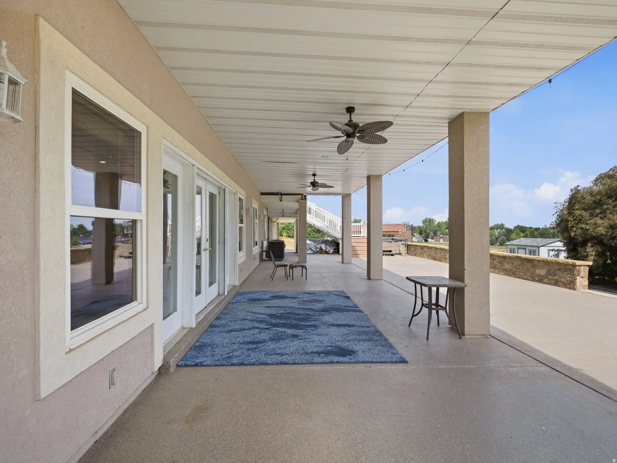 Covered outdoor patio with a concrete surface, featuring multiple ceiling fans, recessed lighting, and access through double French doors