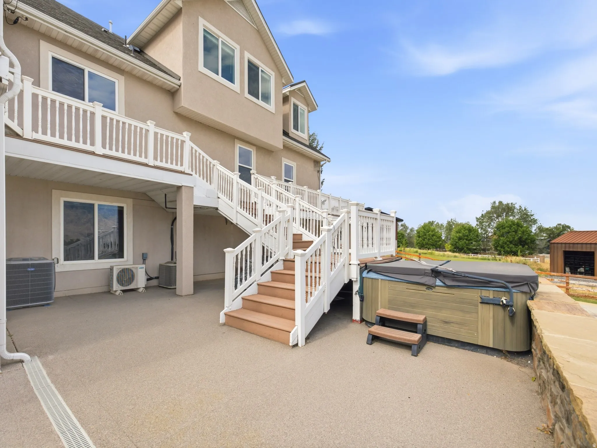 Multi-level rear decking with white railings, a concrete patio, and a covered hot tub