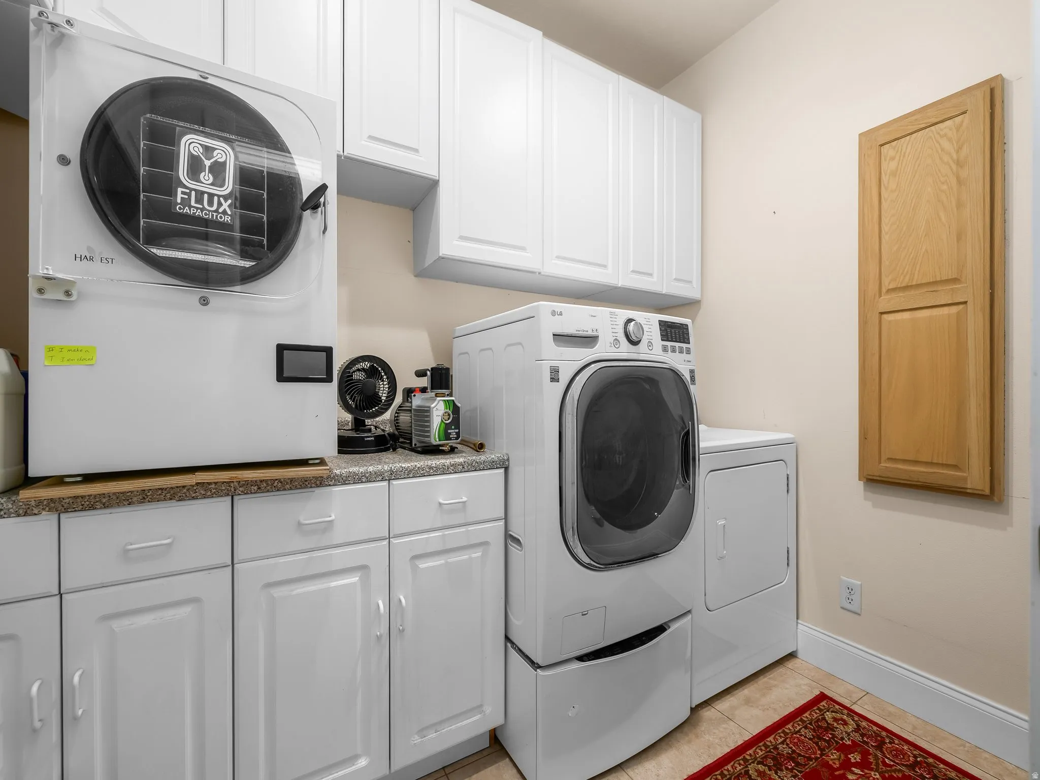Laundry area featuring a front-load washer with pedestal, a dryer, and extensive white cabinetry