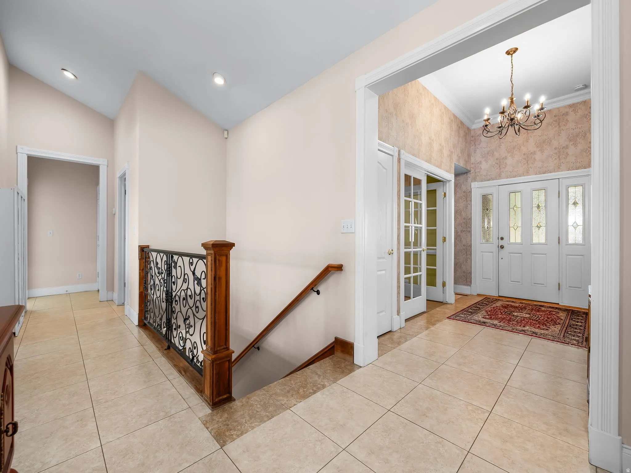 Entryway featuring double doors with decorative glass panels, a high vaulted ceiling, and a wrought iron chandelier