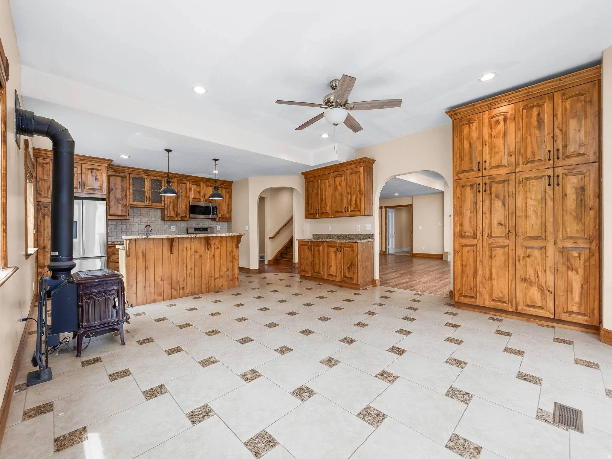 Basement eat in kitchen featuring a wood-burning stove, a kitchen island with seating, extensive wood cabinetry, and a ceiling fan