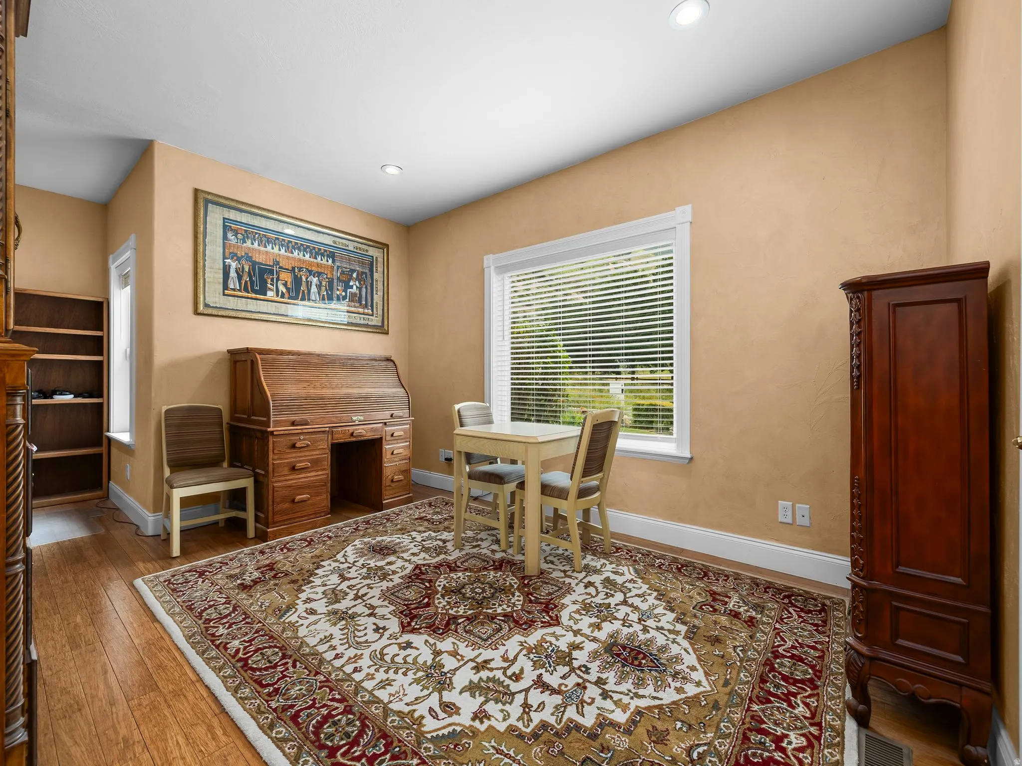 Warmly toned room featuring wood-finish flooring, a built-in shelving unit, and a window with blinds