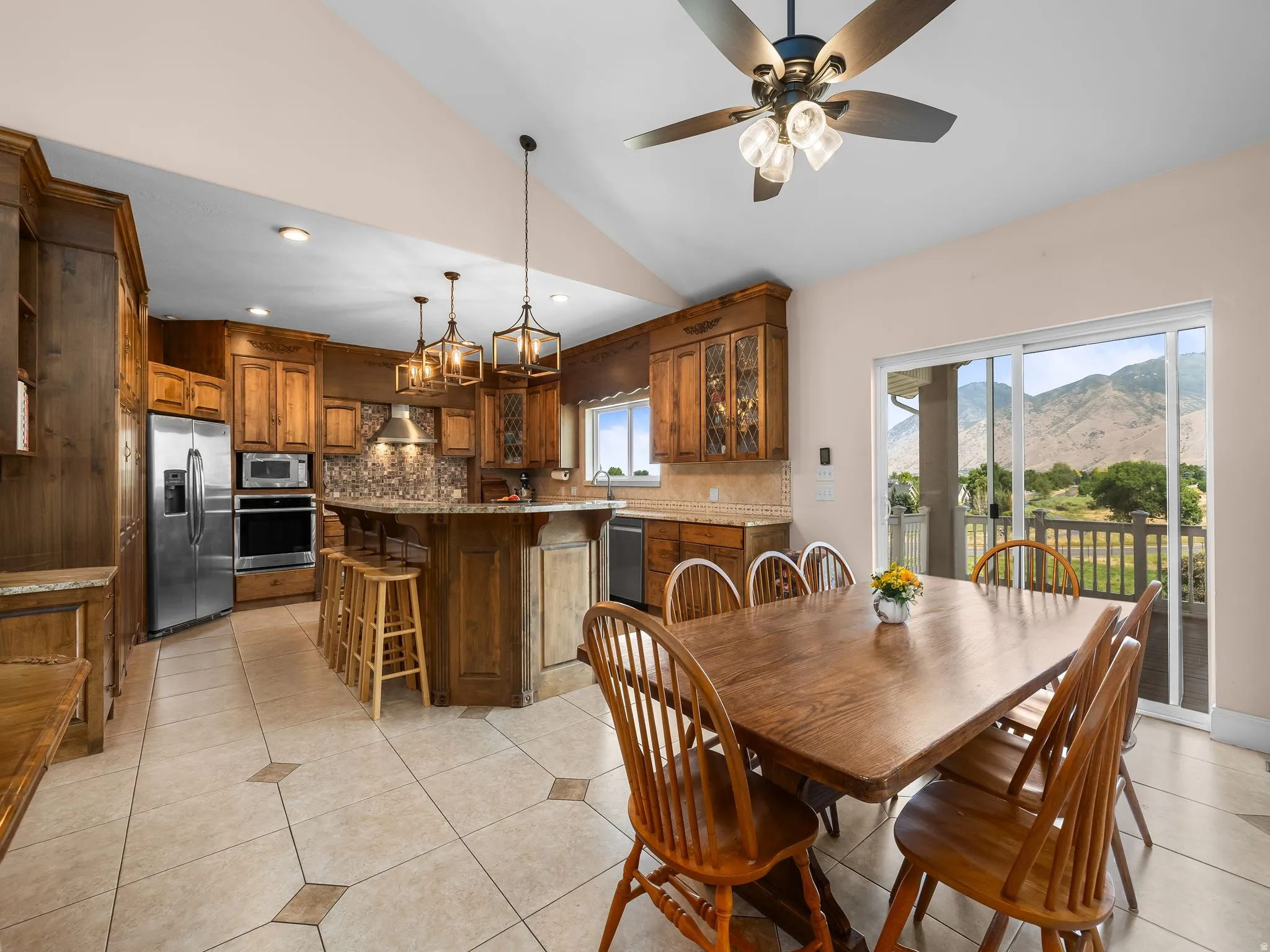 Open-concept kitchen and dining area with vaulted ceilings, featuring wood cabinetry, stainless steel appliances, and a tiled backsplash