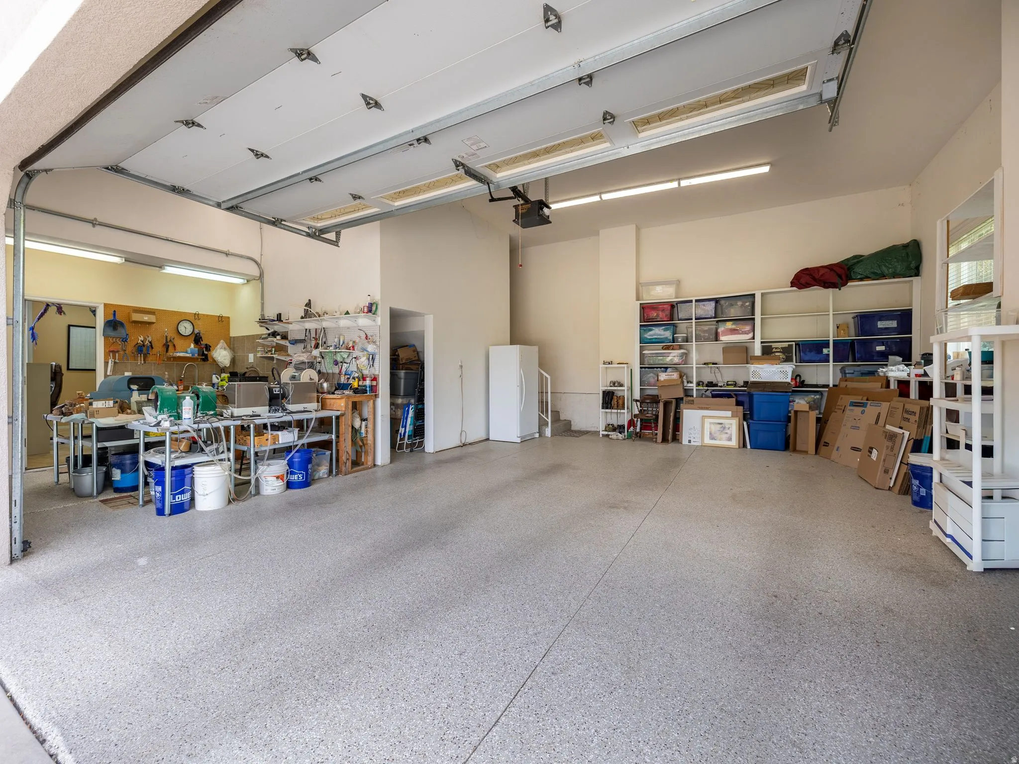 Spacious garage featuring a durable epoxy floor, ample overhead fluorescent lighting, and a dedicated workbench area