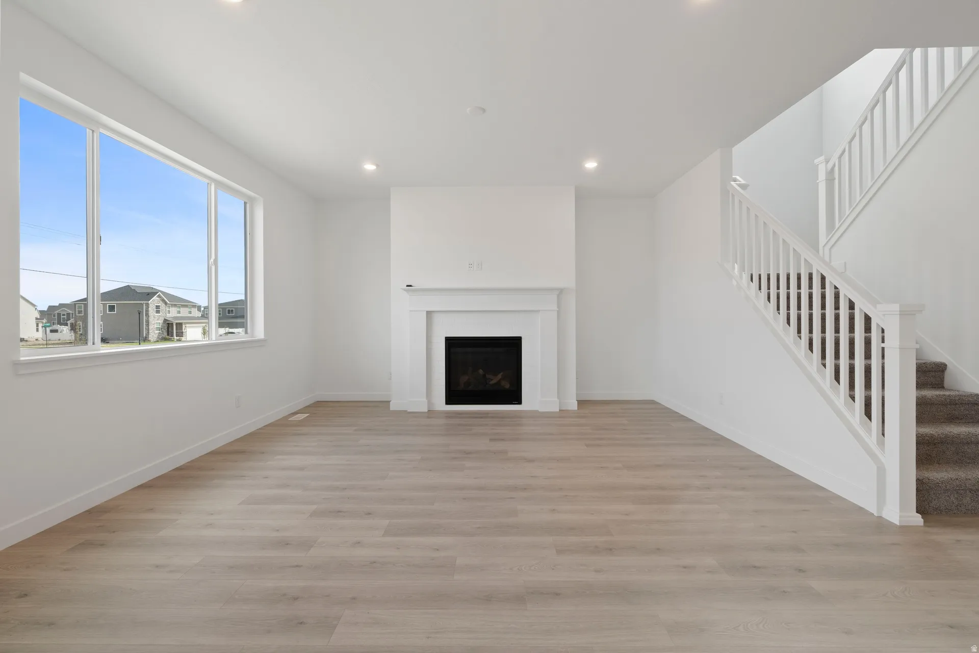 Spacious living area featuring wood-finish flooring, a traditional fireplace with a white mantel, and a bright window
