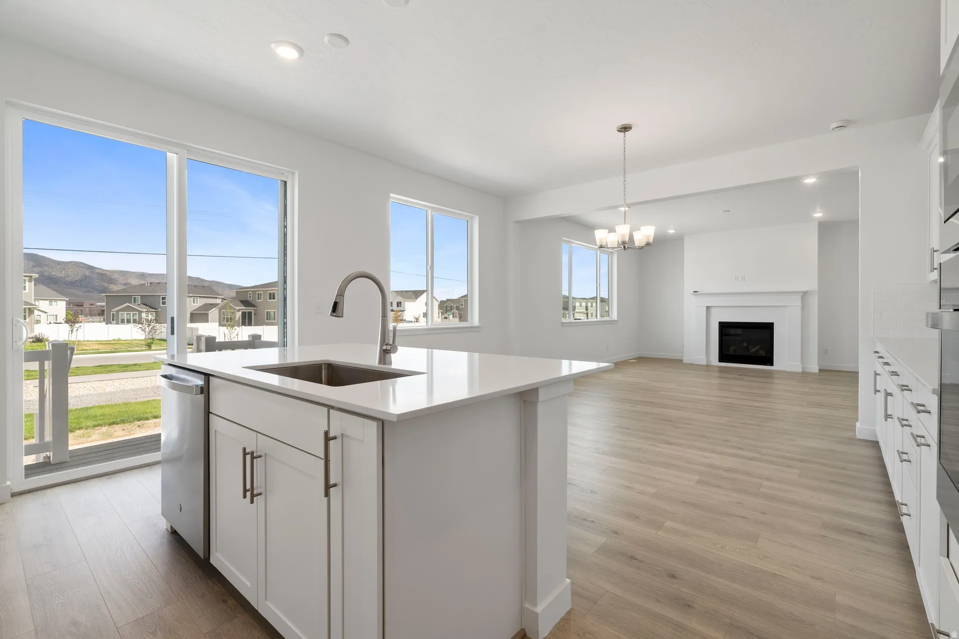 Open-concept living area featuring a kitchen island with a stainless steel sink, a fireplace with a white mantel, wood-finish flooring, and a sliding glass door