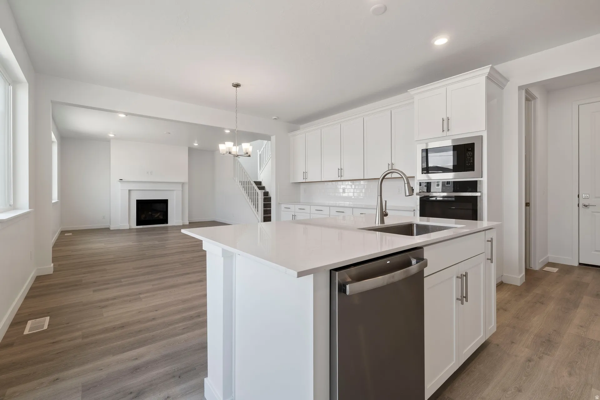 Contemporary kitchen island with a built-in stainless steel sink and dishwasher, quartz countertop, white shaker cabinetry, and wood-finish flooring