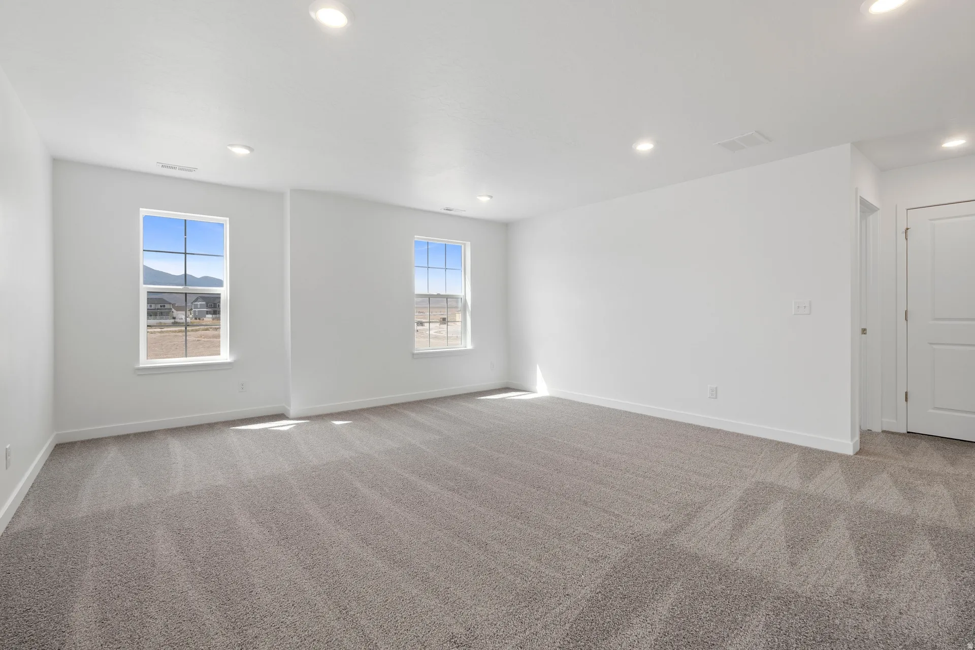 Spacious room featuring neutral carpeting, recessed ceiling lighting, and two windows