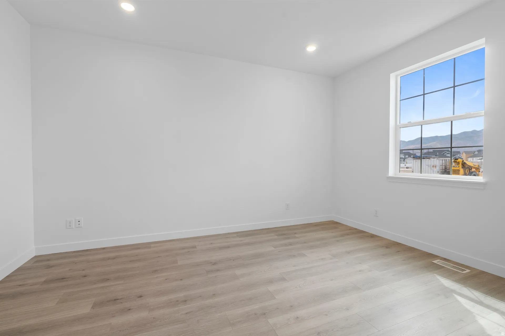 Bright interior space featuring a large window with grid pattern, recessed ceiling lighting, light wood-finish flooring, and white baseboards