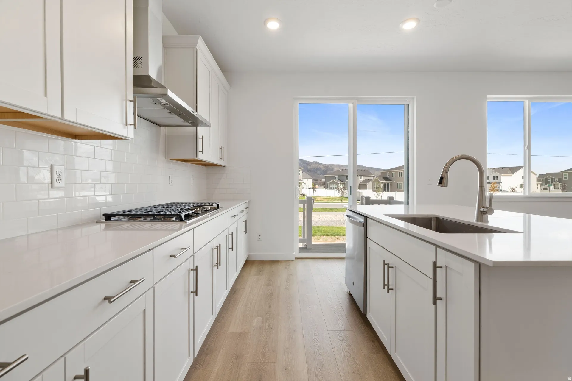 Contemporary kitchen featuring white cabinetry, quartz countertops, a tile backsplash, wood-finish flooring, and a stainless steel sink with a gooseneck faucet