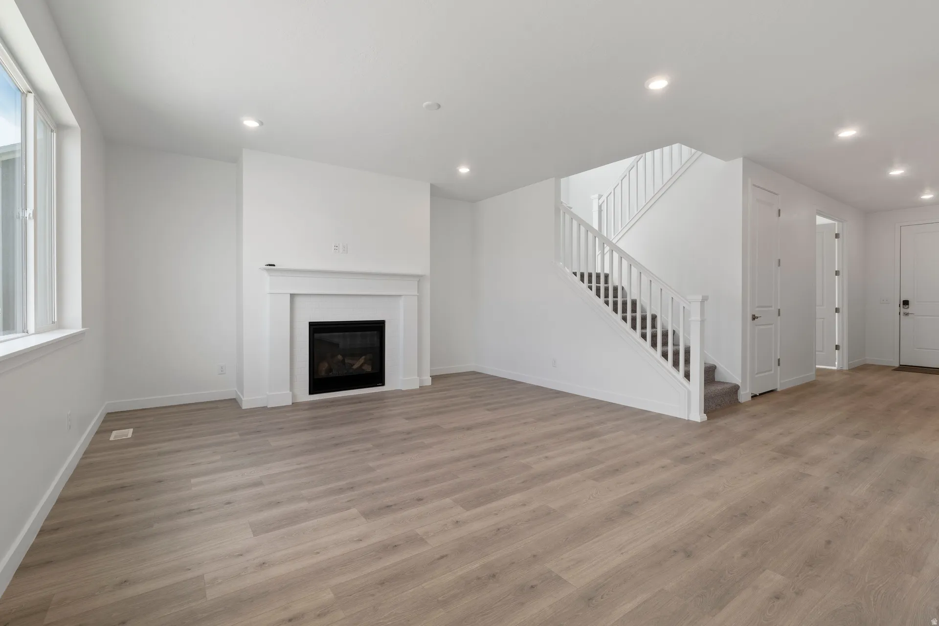 Spacious living area featuring light wood-finish flooring, a white mantel fireplace, and recessed lighting