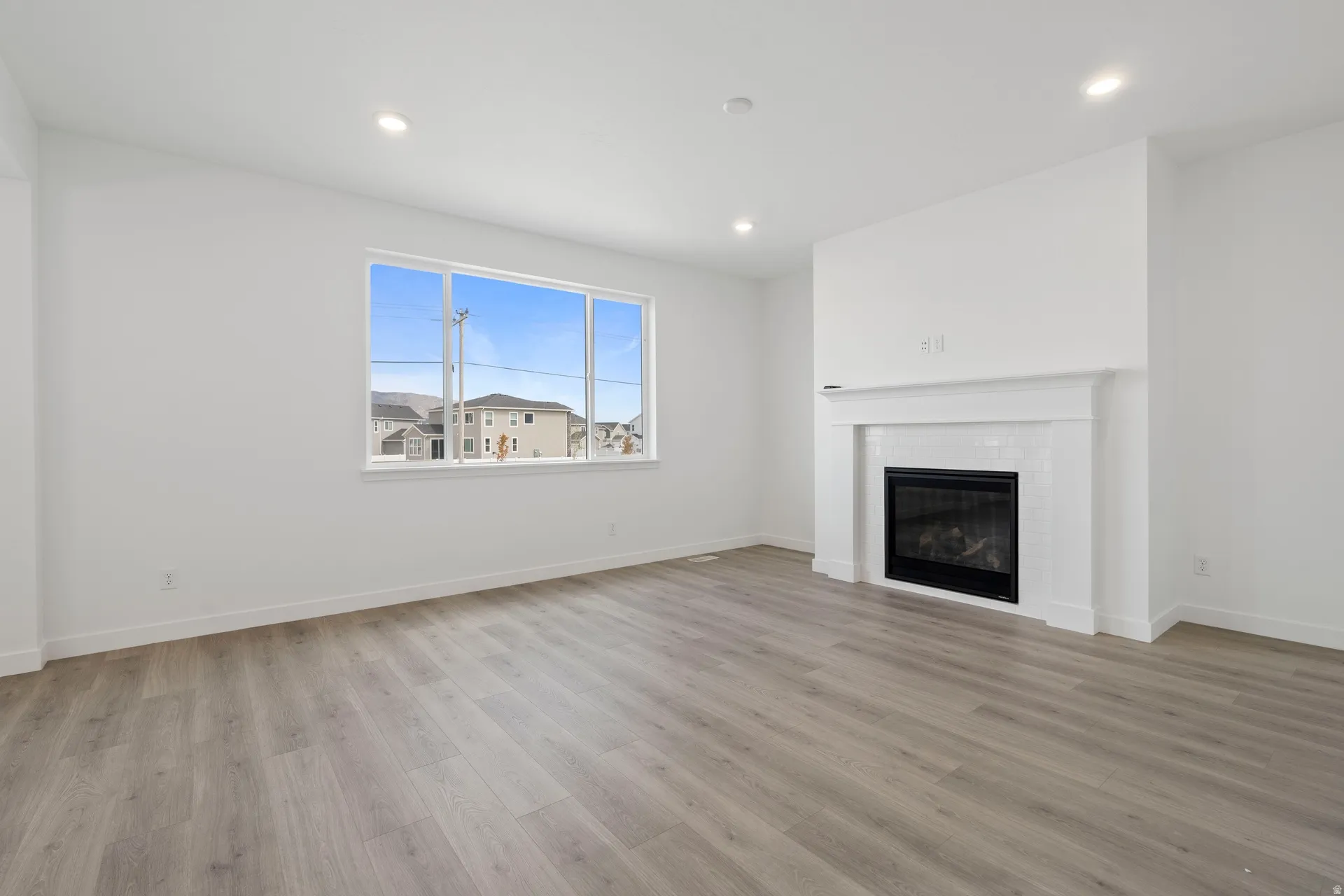 Living area featuring a gas fireplace with a white mantel and subway tile surround, wood-finish flooring, recessed lighting, and a large window