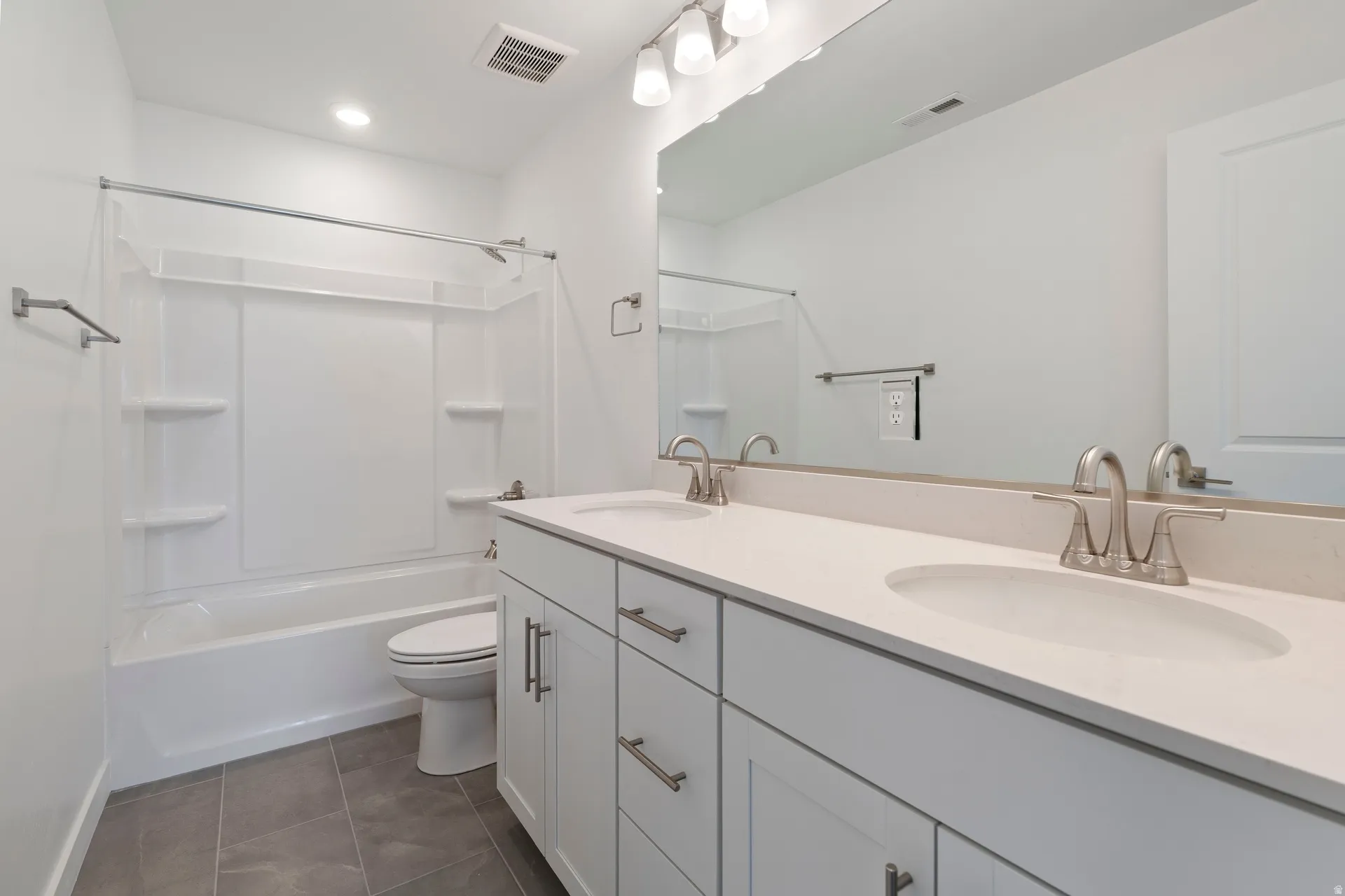Contemporary bathroom featuring a double vanity with light-toned countertops and undermount sinks, brushed nickel fixtures, a full-width mirror, and a white tub/shower combination with integrated shelving