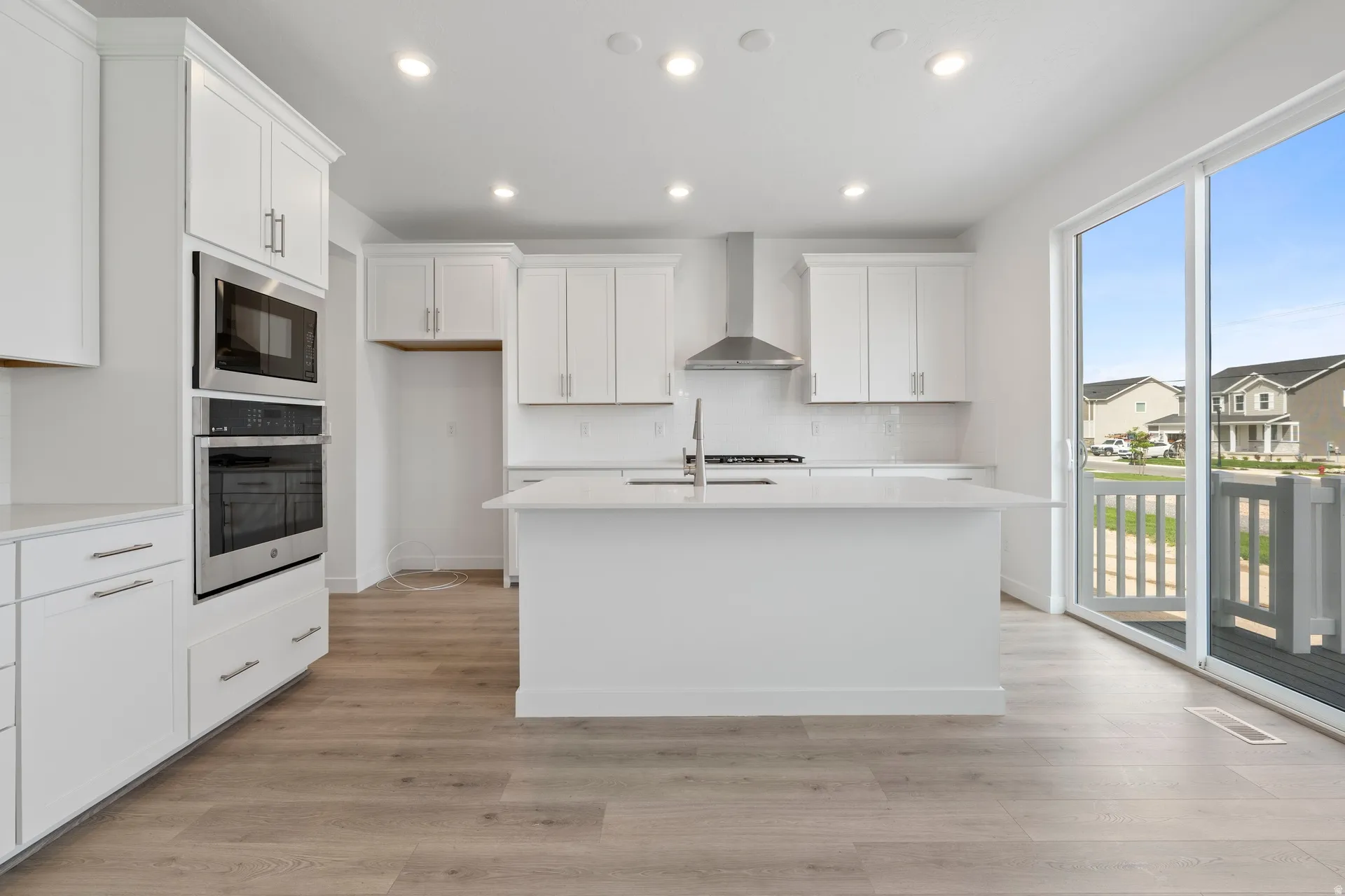 Bright kitchen featuring a central island, white cabinetry, integrated stainless steel appliances, wood-finish flooring, and sliding glass doors