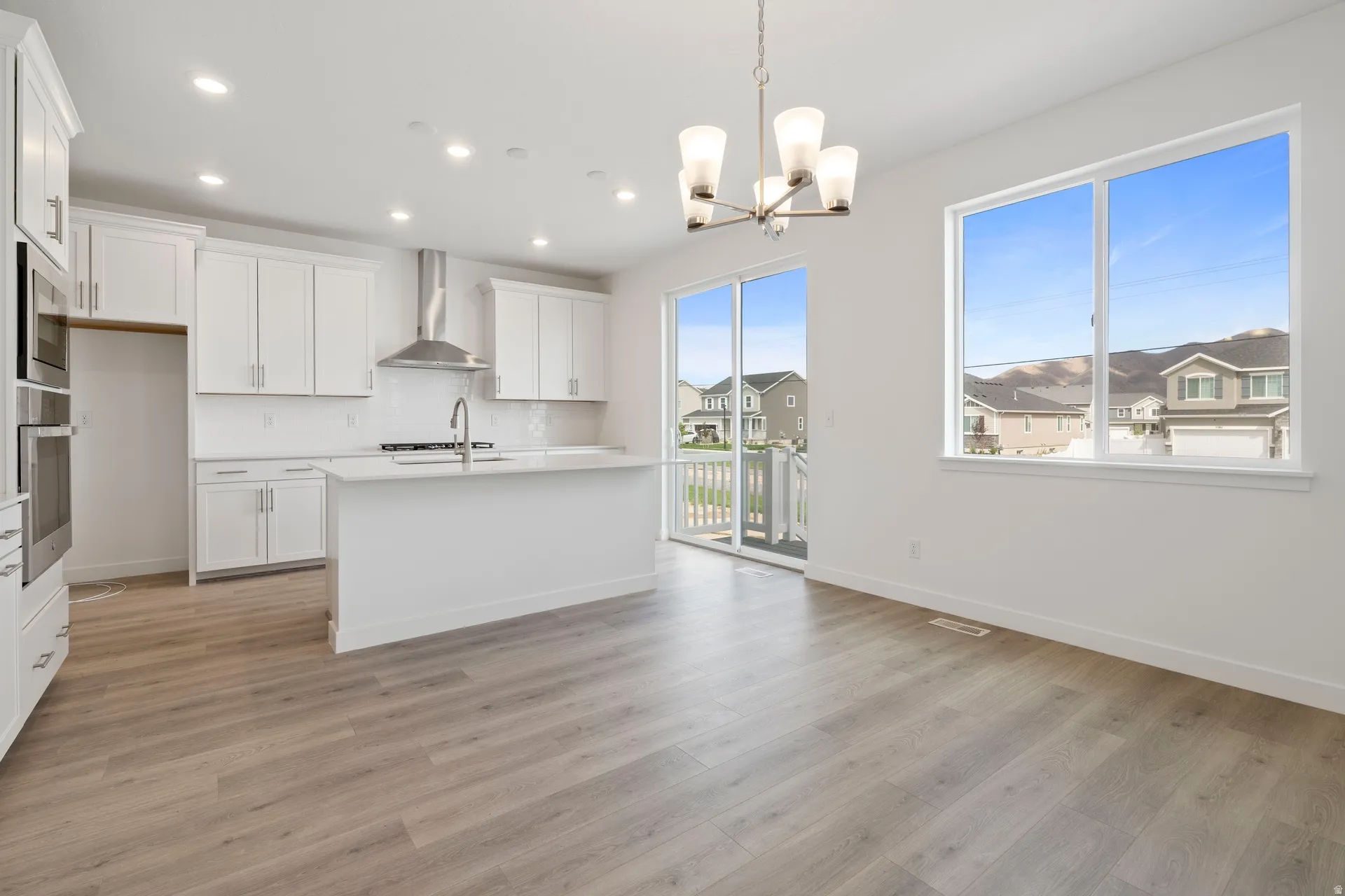 Bright open-concept kitchen and dining area featuring light wood-finish flooring, white cabinetry, a large kitchen island with integrated sink, and stainless steel appliances