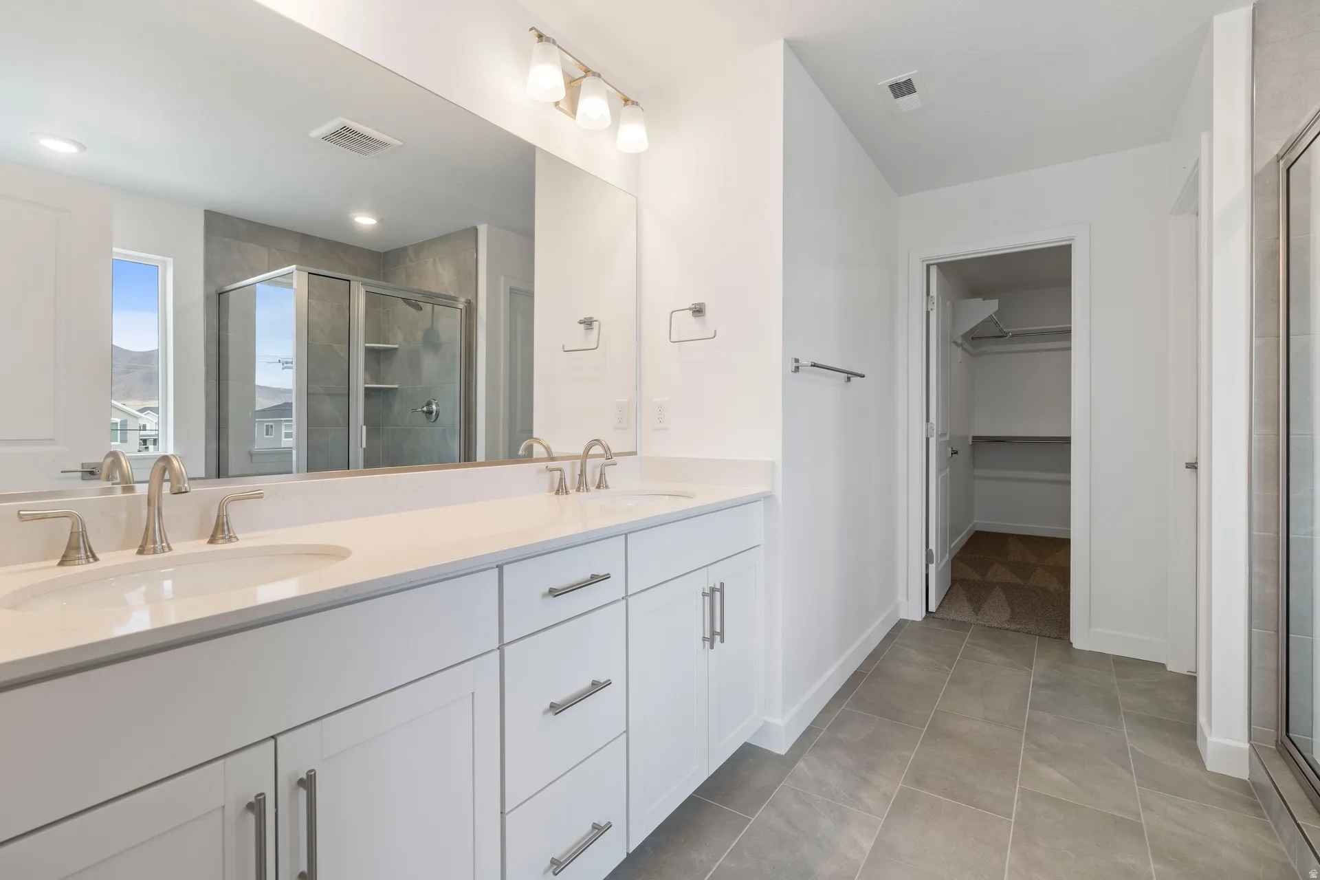 Dual vanity with white cabinetry and brushed nickel hardware, featuring a large mirror and overhead light bar