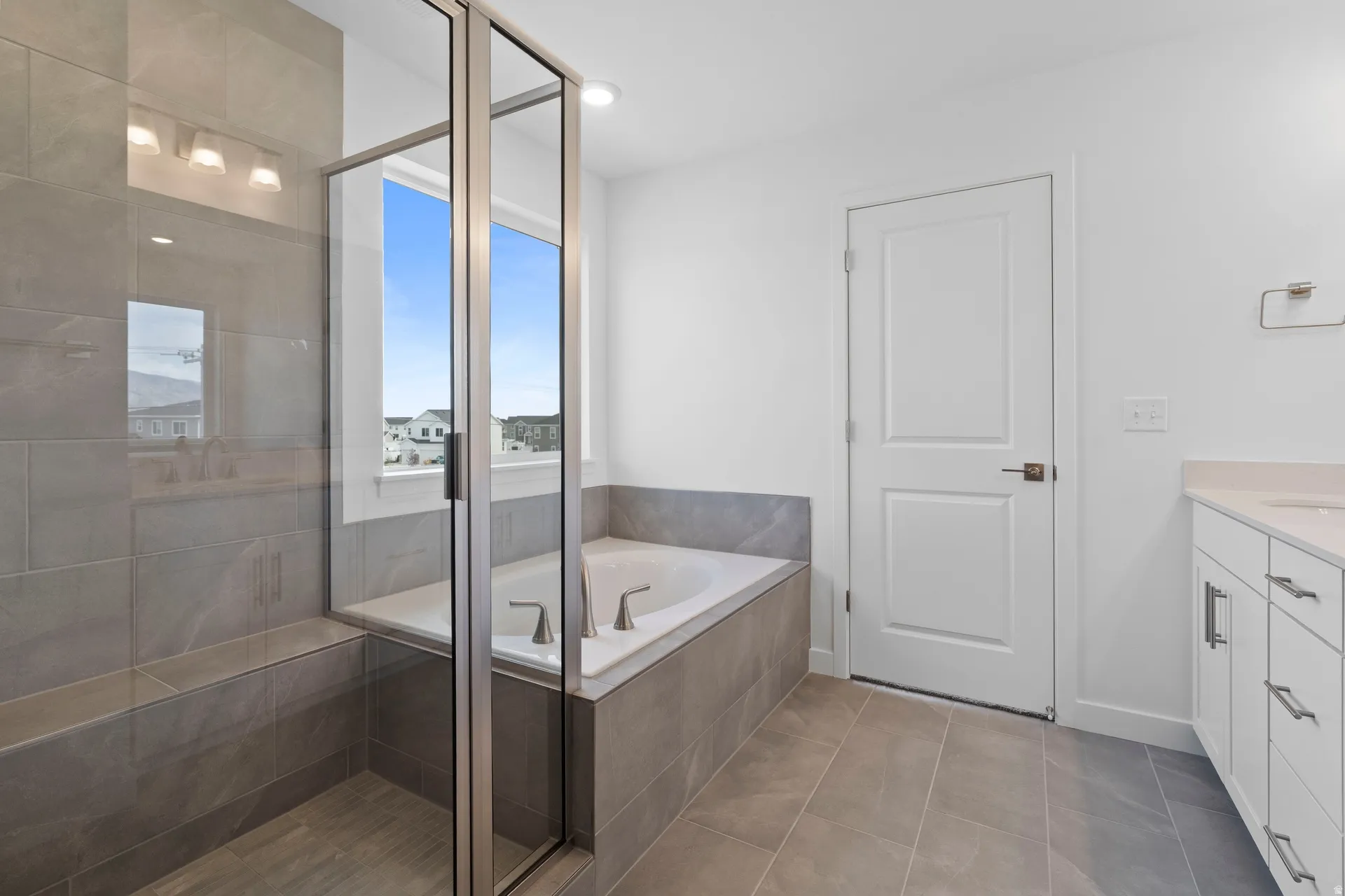 Spacious bathroom featuring a glass-enclosed shower with a built-in bench, a separate soaking tub, and a white vanity with a light-toned countertop