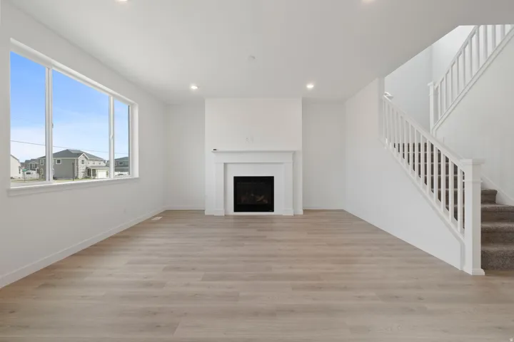 Spacious living area featuring wood-finish flooring, a traditional fireplace with a white mantel, and a bright window