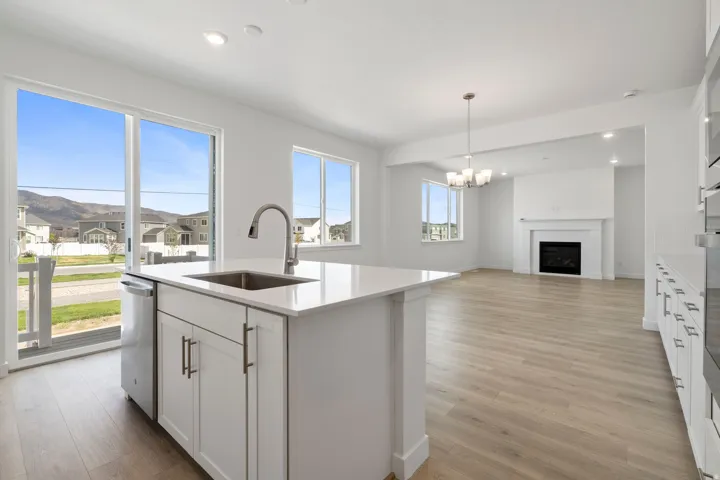 Open-concept living area featuring a kitchen island with a stainless steel sink, a fireplace with a white mantel, wood-finish flooring, and a sliding glass door
