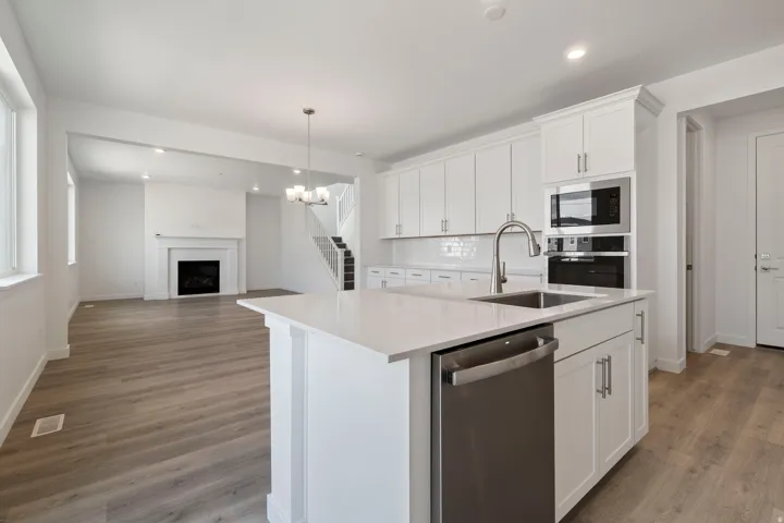 Contemporary kitchen island with a built-in stainless steel sink and dishwasher, quartz countertop, white shaker cabinetry, and wood-finish flooring