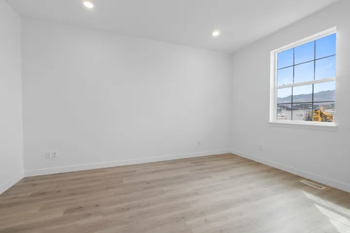 Bright interior space featuring a large window with grid pattern, recessed ceiling lighting, light wood-finish flooring, and white baseboards