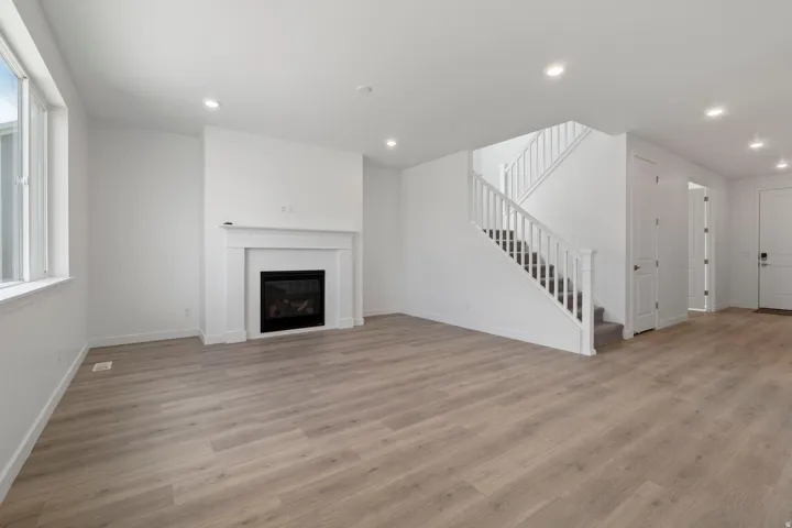 Spacious living area featuring light wood-finish flooring, a white mantel fireplace, and recessed lighting