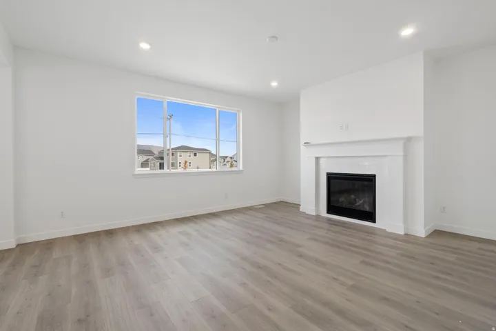 Living area featuring a gas fireplace with a white mantel and subway tile surround, wood-finish flooring, recessed lighting, and a large window