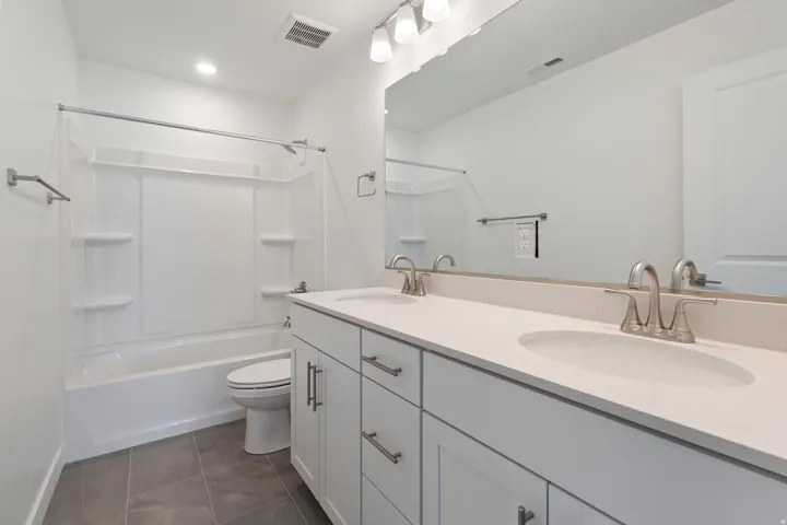 Contemporary bathroom featuring a double vanity with light-toned countertops and undermount sinks, brushed nickel fixtures, a full-width mirror, and a white tub/shower combination with integrated shelving