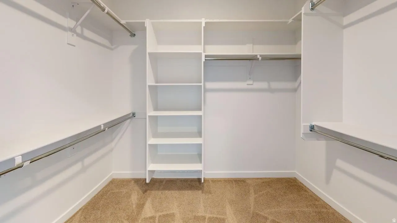 Walk-in closet featuring built-in shelving, multiple hanging rods, white walls, and carpet flooring
