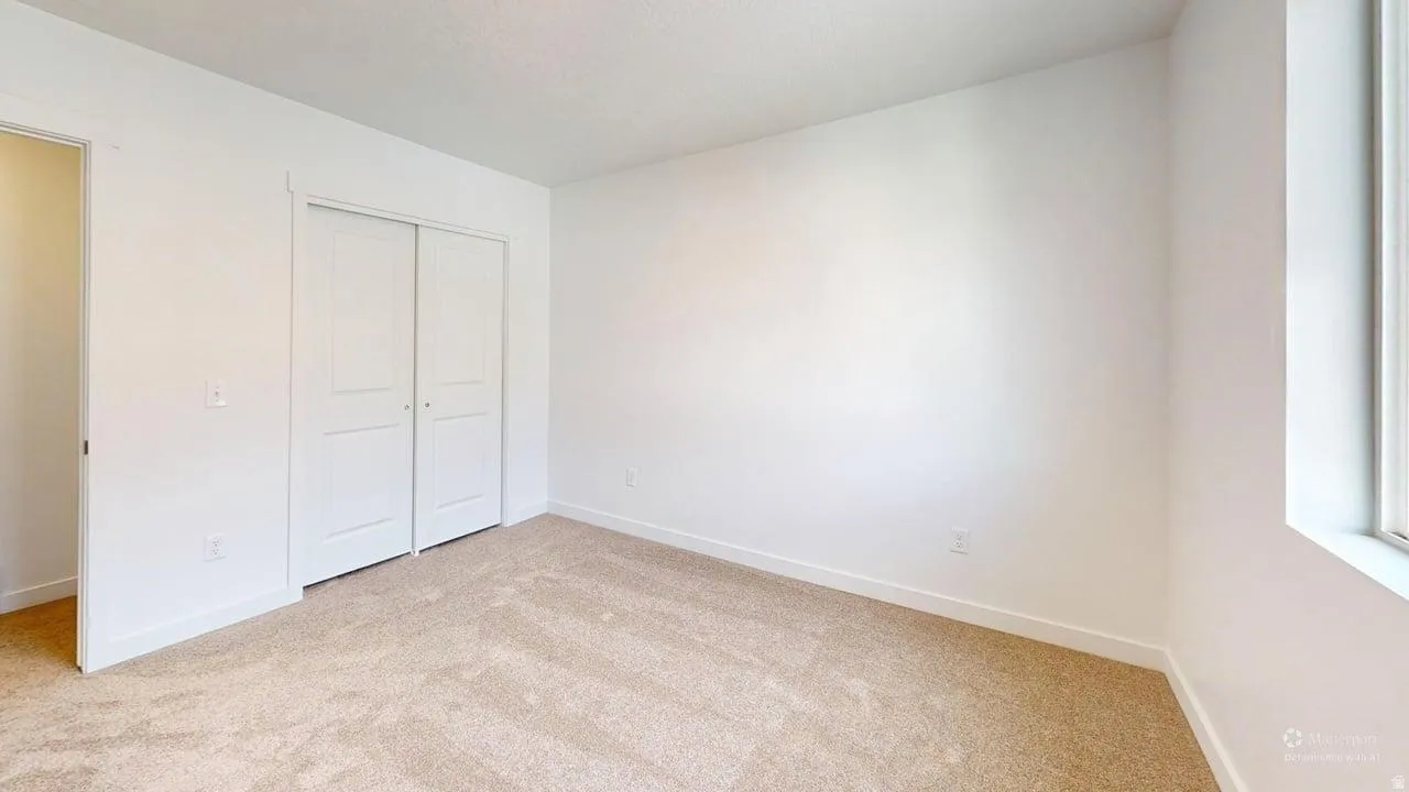 Carpeted room featuring a double-door closet, white trim, and a window for natural light