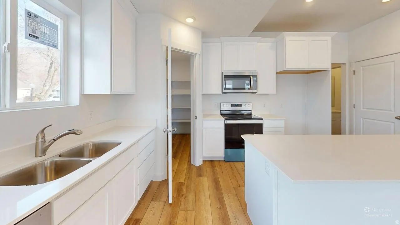 Bright kitchen featuring white cabinetry, light countertops, wood-finish flooring, a stainless steel double sink, and a stainless steel microwave