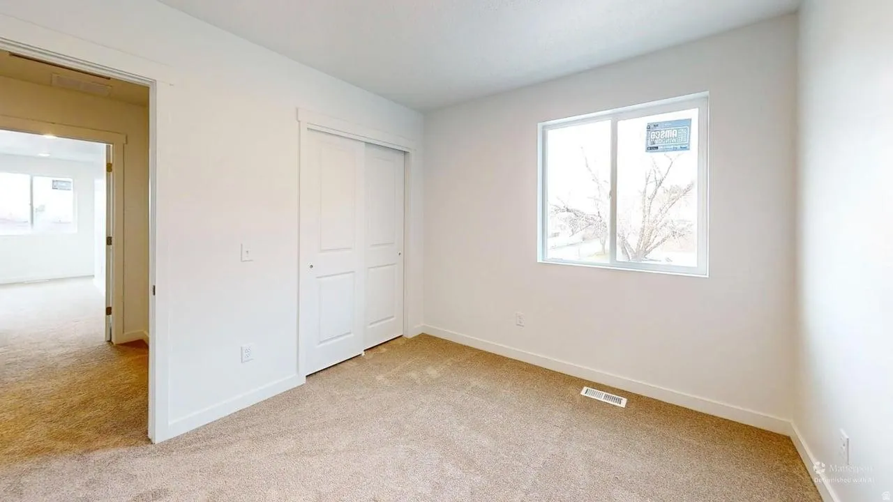 Bright interior room featuring a neutral color palette, plush carpeting, a wide window, and a white sliding closet door