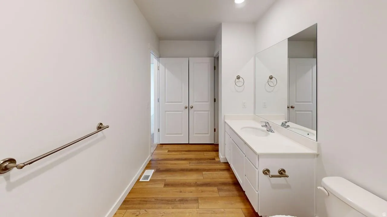 Bathroom featuring a white vanity with an integrated sink, a large wall-mounted mirror, and wood-finish flooring