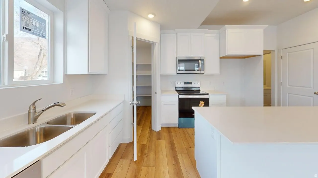 Modern kitchen featuring white cabinetry, light-toned countertops, stainless steel appliances, and wood-finish flooring