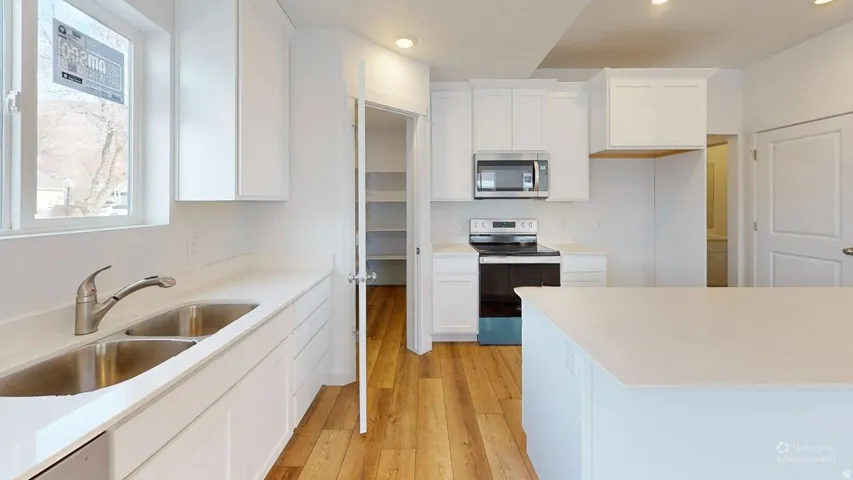 Bright kitchen featuring white cabinetry, light countertops, wood-finish flooring, a stainless steel double sink, and a stainless steel microwave