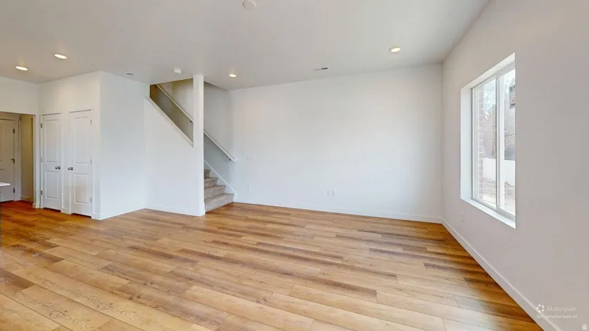 Spacious interior featuring wood-finish flooring, recessed lighting, a multi-pane window, and a staircase with carpeted treads